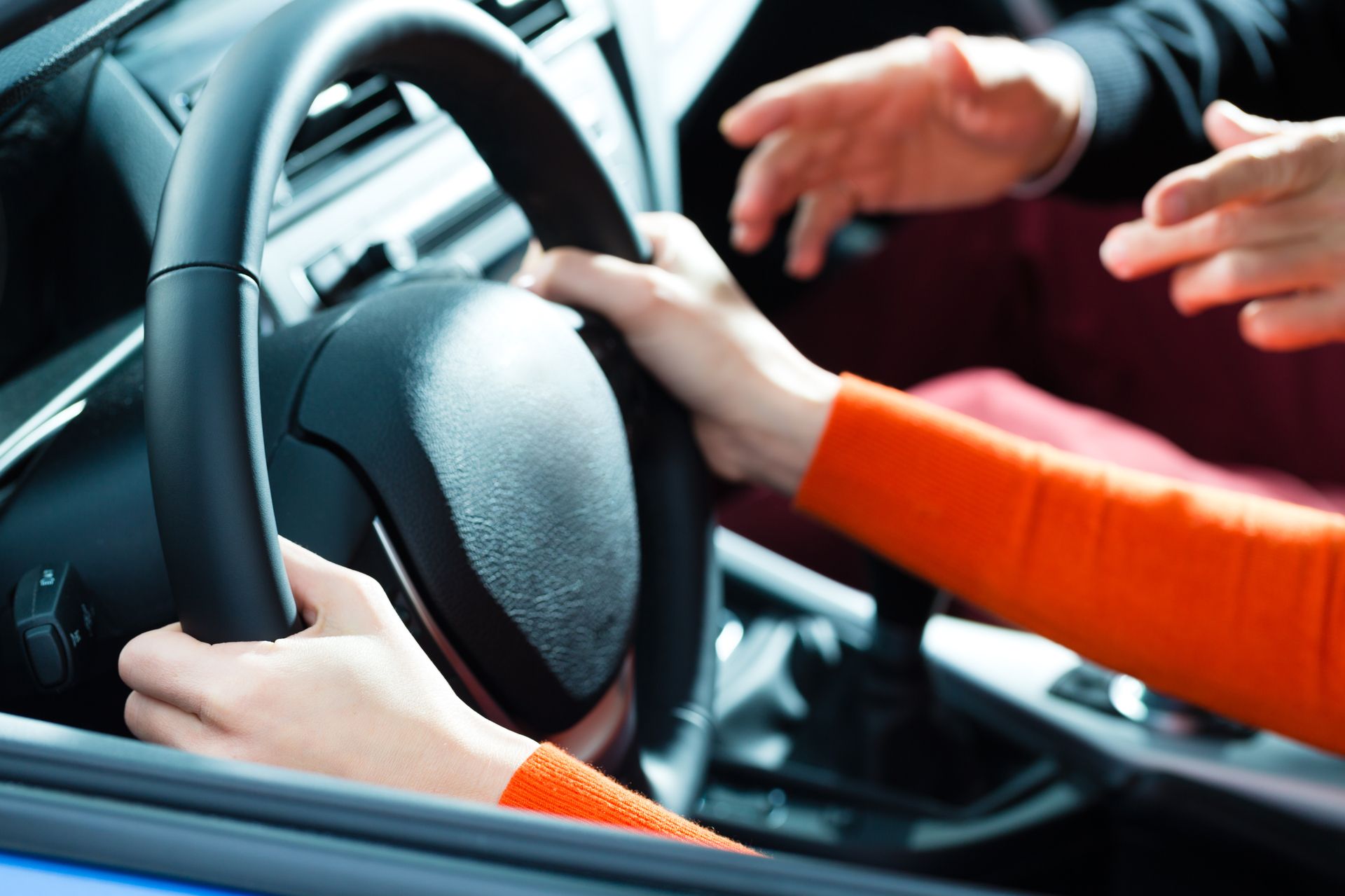 Nahaufnahme von zwei Personen im Auto, eine hält das Lenkrad, die andere gestikuliert mit beiden Händen